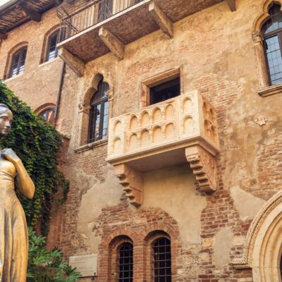Gold-painted statue of a woman in front of an ivy-covered brick building with arched windows and a decorative balcony.