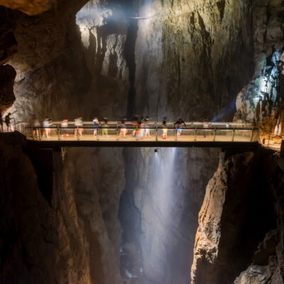 Suspended walkway in a limestone cave, with visitors along a railing above a deep chasm.